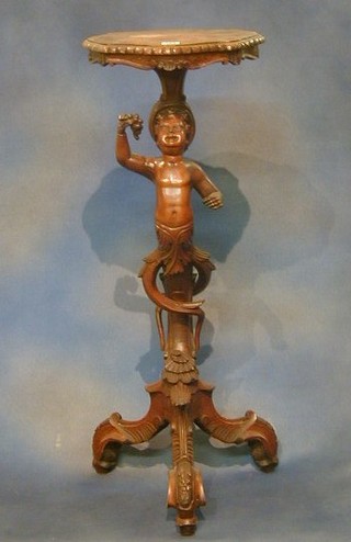 A 19th Century Continental carved walnutwood torchere supported by a figure of a cherub with bunch of grapes raised on tripod supports