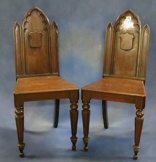 A pair of Victorian mahogany Gothic hall chairs with solid seats raised on turned chamfered supports