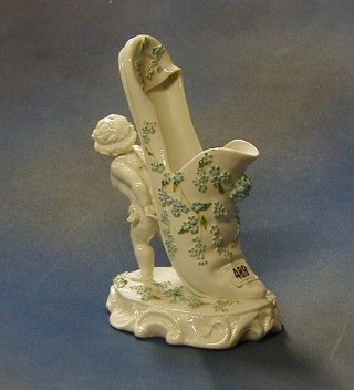 A Victorian Continental porcelain vase in the form of a slipper supported by a cherub 10"