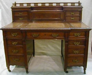 A Victorian carved mahogany breakfront pedestal kneehole writing desk, the upper section with pierced three-quarter gallery and having centre stationery box with hinged lid flanked by a 4 short drawers, the top inset a tooled leather writing surface with hinged lid revealing a fitted interior, above 1 long and 8 short drawers with fluted decoration 53"