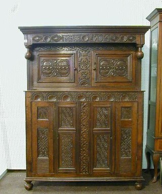 An early 18th Century carved oak court cupboard, the upper section fitted a double cupboard enclosed by panelled doors, the base fitted a double cupboard and enclosed by panelled doors marked MRA 704 50"