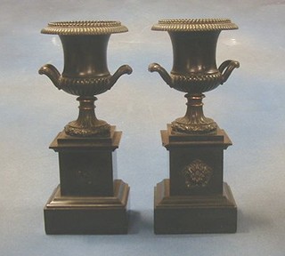 A pair of bronze twin handled urns raised on marble plinths 11"