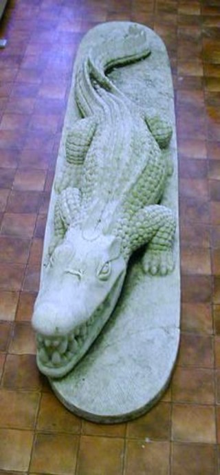 A life sized carved stone figure of a crocodile 71", raised on an oval base (crack to base)