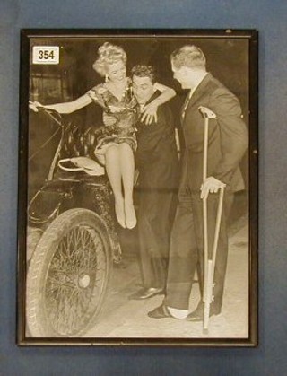 A 1950's/60's black and white photograph of Bob Monkhouse lifting a lady from a vintage motorcar and 1 other gentleman 15" x 11"