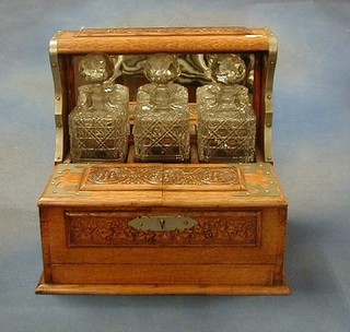 An Edwardian honey oak 3 bottle tantalus with silver banding, the base fitted a cigar box and secret drawer with a cribbage board