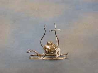 A silver plated brandy warmer in the form of a burner raised on a pair of skis