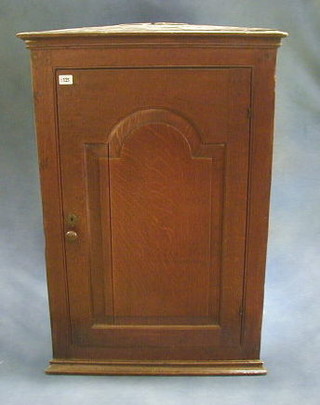 A Georgian Country oak hanging corner cabinet with moulded cornice, fitted adjustable shelves enclosed by an arched panelled door, 26"