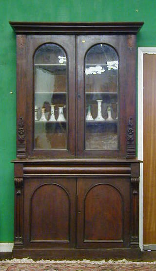 A Victorian mahogany bookcase on cabinet the upper section with moulded cornice, fitted adjustable shelves enclosed by arched glazed panelled doors, the base fitted 1 long drawer above a double cupboard, raised on a platform base 50"