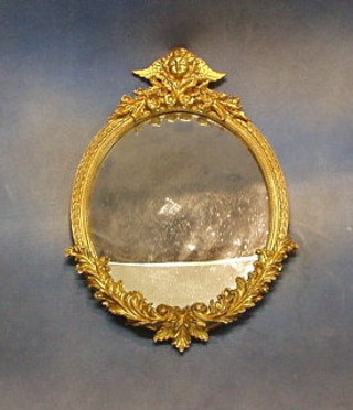 A 19th/20th Century oval plate wall mirror contained in a decorative gilt frame surmounted by a figure of a winged cherub 21"