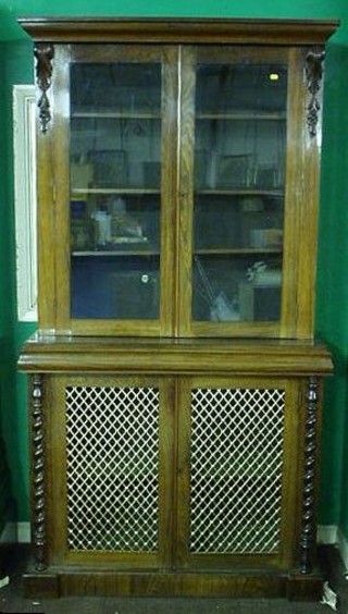 A Victorian rosewood bookcase on cabinet, the upper section with moulded cornice and Vitruvian scroll decoration to the sides, fitted adjustable shelves enclosed by glazed panelled doors, the base fitted a cupboard enclosed by brass grilled panelled doors and having spiral turned columns to the sides 44"