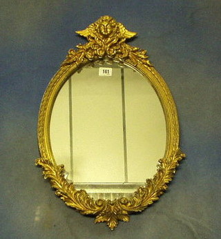 A 19th/20th Century oval plate wall mirror contained in a decorative gilt frame, surmounted by a figure of a winged cherub 21"