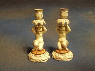 A pair of 19th Century Continental porcelain candlesticks in the form of cherubs supporting sconces, 9"