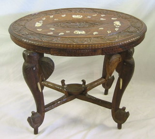 An oval Eastern carved hardwood table,  raised on elephant supports with X framed stretcher, the top inlaid elephants and camels, 31"