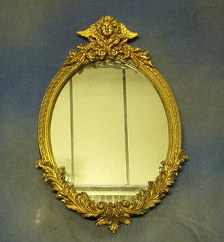 A 19th/20th Century oval plate wall mirror in a decorative gilt frame, surmounted by a figure of a cherub 21"