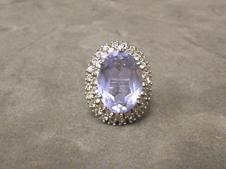 A lady's white metal dress ring set an oval blue cut stone surrounded by brilliants