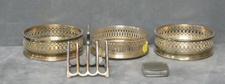 3 circular pierced silver plated wine coasters, a silver plated toast rack and a pill box