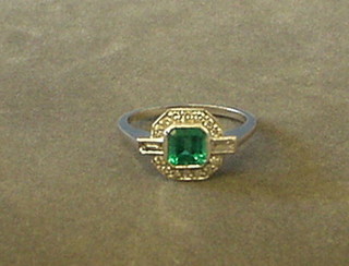 A lady's white gold dress ring set an octagonal cut emerald surrounded by numerous diamonds and with 2 baguette cut diamonds to the shoulders