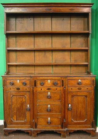 A Georgian oak breakfront dresser, the raised back with moulded cornice above 3 shelves, the base fitted 4 long drawers flanked by a pair of cupboards with ivory escutcheons and tore handles, raised on bracket feet 56"