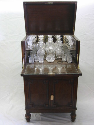 A 1930's oak Jacobean style cocktail cabinet, the interior fitted 5 cut glass decanters, 4 cut glass martini glasses, 2 sherry glasses, 2 liqueur glasses, 5 large whisky decanters, 4 small whisky decanters and a circular nut dish, the base fitted a double cupboard with cellarette drawer enclosed by panelled doors and raised on bun supports 26"