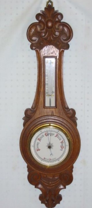 A 19th/20th Century aneroid barometer and thermometer with porcelain dial contained in a carved oak wheel case