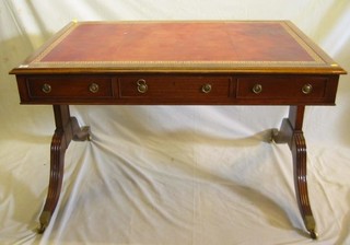 A Georgian style mahogany library table with inset tooled  red leather writing surface, fitted 3 drawers, raised on splayed supports ending in brass caps and castors, 48"