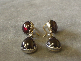 A pair of lady's drop earrings set circular cabouchon cut garnets and a diamond above a tier drop cabouchon garnet