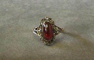 A lady's gold dress ring set an oval cabouchon cut garnet surrounded by 16 diamonds