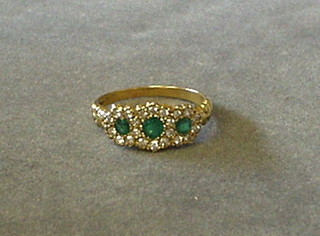 A lady's gold dress ring set 3 emeralds surrounded by numerous diamonds