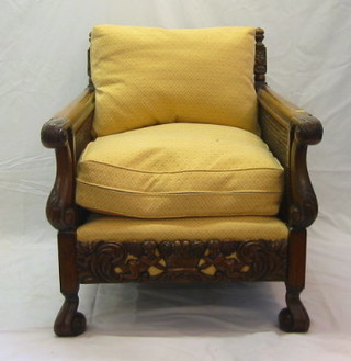 A pair of 19th/20th Century carved oak double cane bergere chairs with cresting rails carved cherub and basket, having upholstered seats and on French cabriole supports