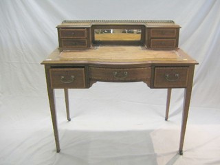 An Edwardian inlaid and crossbanded mahogany writing table, the inverted break front upper section with pierced brass three-quarter gallery fitted a mirror flanked by 4 short drawers, the bow front base fitted 1 long and 2 short drawers, raised on square tapering supports ending in ceramic castors, 40"