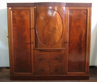 An Edwardian mahogany triple breakfront wardrobe with blind fret work cornice, fitted a linen press section to the centre above 2 long drawers, flanked by a pair of cupboards, raised on a platform base