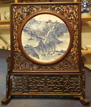 A circular Oriental blue and white porcelain plaque contained in a pierced hardwood table screen