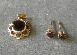 A gold pendant set an oval cut red stone and a pair of ear studs
