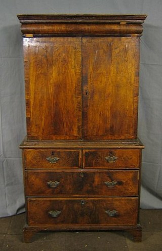 A Queen Anne walnutwood cabinet on chest, the top with moulded cornice fitted a cushion shaped secret drawer, the cupboard enclosed by a panelled door fitted 8 short and 1 long drawers, enclosed by panelled doors with feather banded decoration, the base fitted 2 short and 2 long drawers with brass plate swan neck drop handles, raised on bracket feet (removed from a Sussex Country House) 37"