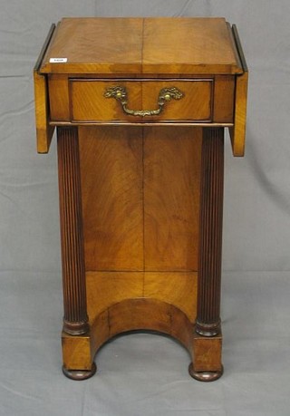 An Empire style walnutwood drop flap bedside table fitted a drawer, raised on turned and reeded supports with concave base, raised on bun feet, 17"