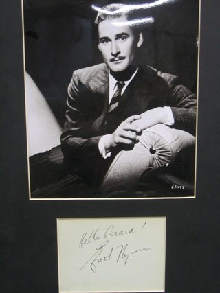 A black and white portrait photograph of Errol Flynn on a couch, mounted together with a signature "Hello Friend"