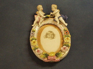 A "Dresden" oval porcelain frame surmounted by 2 figures of cherubs with floral encrustation 6" (f)