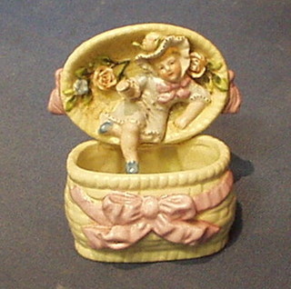 A 19th Century Continental ornament in the form of a child emerging from a lidded basket 6"