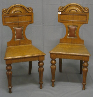 A pair of Edwardian carved honey oak hall chairs with solid seat backs 