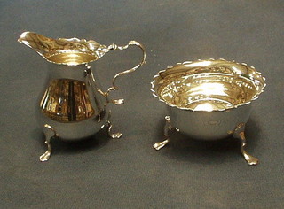 A modern silver sugar bowl with cut border, raised on 3 hoof feet together with a matching cream jug, hallmarked Birmingham, 6 ozs