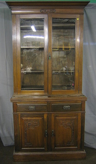 An Edwardian Art Nouveau walnutwood bookcase on cabinet, the upper section with moulded cornice, the interior fitted adjustable shelves enclosed by glazed panelled doors, the base fitted 2 long drawers above a double cupboard enclosed by carved panelled doors, raised on a platform base 42"