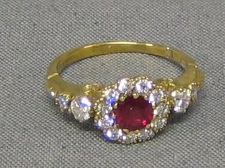 A lady's gold dress ring set a circular cut ruby surrounded by 11 diamonds and 4 diamonds to the shoulders