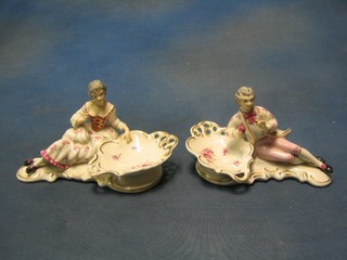 A pair of 20th Century Continental porcelain salts supported by a figure of a lady and gentleman climbing, the base with crowned M and impressed 208OH 7"