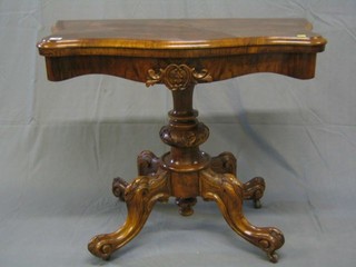 A Victorian figured walnutwood card table of serpentine outline raised on a carved florette bulbous column and tripod supports 36"