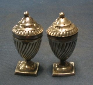 A pair of Victorian silver pepperettes of urn form with demi-reeded decoration, raised on square feet, Chester 1883,