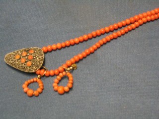A string of coral beads, a pair of coral earrings and a dress clip