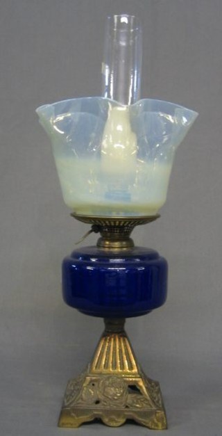 A 19th/20th Century blue glass oil lamp reservoir, raised on a pierced gilt metal base with vaseline glass shade