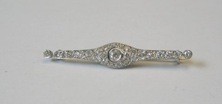 An 18ct white gold bar brooch set a circular cut diamond supported by numerous diamonds (approx 0.6ct)