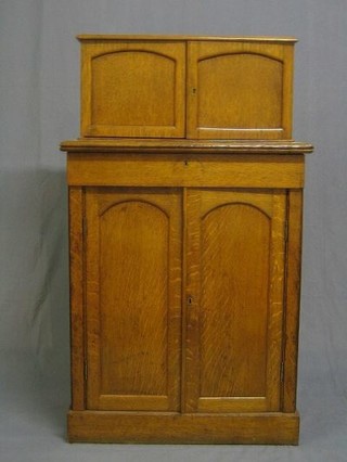 A Victorian honey oak cabinet on cabinet, the upper section fitted double cupboard enclosed by arched panelled doors, the base fitted 1 long drawer above a double cupboard enclosed by arched panelled doors, raised on a platform base, 30"