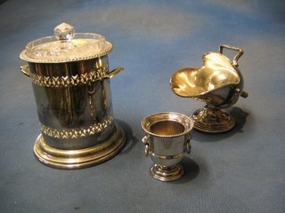 A silver plated sugar scuttle, a circular pierced silver soda siphon holder, a cut glass biscuit barrel and cover and a silver match holder in the for of an urn